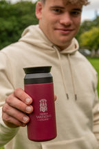 A person in a beige hoodie holds up a dark red insulated water bottle with a black lid. The bottle features the George Watson's College crest and name printed in white.