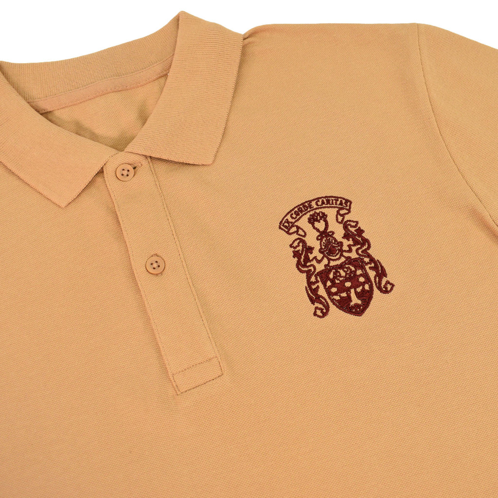 A close-up of a tan polo shirt featuring a dark red embroidered crest on the left chest with the text 'ST. CUBAN CANVAS'.