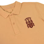A close-up of a tan polo shirt featuring a dark red embroidered crest on the left chest with the text 'ST. CUBAN CANVAS'.